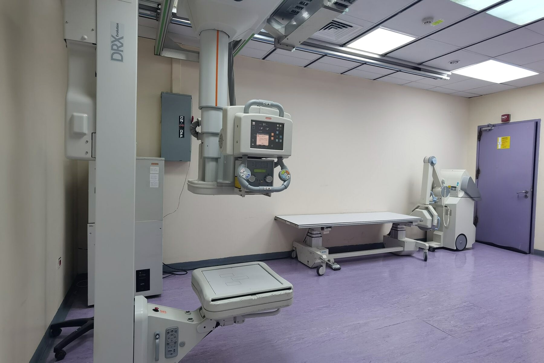 An X-ray room with a ceiling-mounted tube, patient table and wall stand.